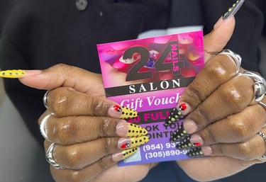 Hand with stiletto acrylic nails featuring yellow and black polka dot nail art holding a 24 Nails Salon gift voucher.