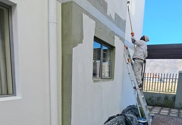 Professional painter applying white exterior paint to a multi-story building using a roller and ladder.