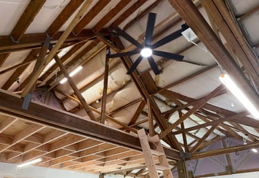 Exposed wooden roof trusses in a garage attic with a black ceiling fan and bright LED lights.
