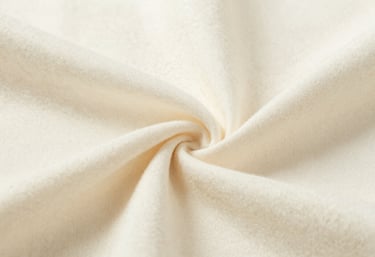 A macro shot of high-quality, soft cotton fabric in a creamy off-white color, showing the fine texture and durability of children's clothing materials.