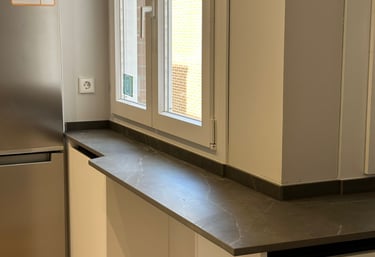 Ventana de cocina, encimera oscura, muebles blancos.