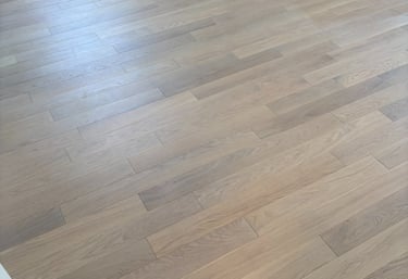 A wide shot of light oak hardwood flooring with a smooth matte finish in a bright modern room. 