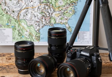 Professional camera gear, including lenses and a tripod, sitting on a rustic wooden table next to a detailed topographical map of a US mountain trail.
