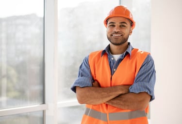 Um engenheiro elétrico usando colete e capacete de segurança sorrindo e com braço cruzado