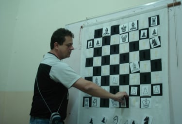 Reinaldo Mano movendo uma peça num quadro tabuleiro durante uma aula