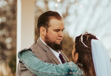 Groom in a grey suit and a bride in a denim jacket share a romantic moment during a gazebo wedding ceremony.
