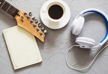 Guitare, tasse de café, casque audio, et cahier posés sur une table.