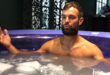 Bearded man sits in a portable ice bath tub for cold water immersion recovery.
