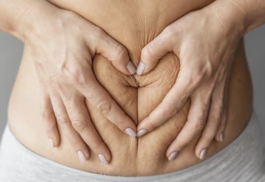 a woman's hands making a heart shape with her hands on her stomach