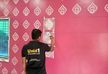 Professional painter applying a white damask stencil pattern on a pink interior accent wall.