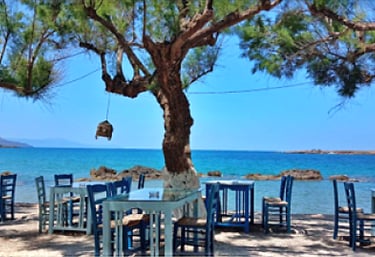 a table with chairs and tables in front of a tree in chania