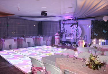 Salón elegante con pista de baile iluminada, mesas decoradas y detalles florales.