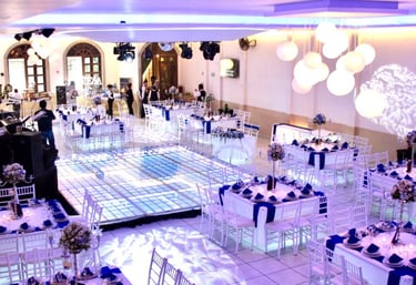 "Evento nocturno con mesas decoradas en tonos oscuros, luces y ambiente elegante.