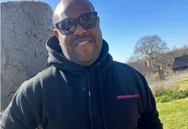 Man outside in a sweater and glasses looks at the camera.