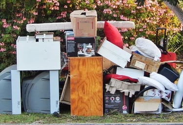 junk on a curb in front of a house consisting of a piece of furniture, garbage bags, pillows, TVs