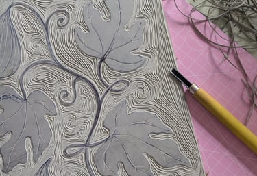 a linocut block of figs being carved out with linocut tools on desk