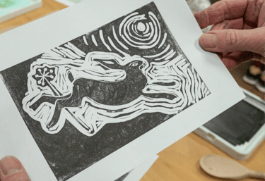 Person holding a linocut print of a hare with art workshop in background