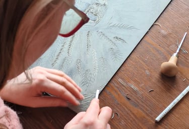 Artist carving an intricate botanical linocut print on a grey lino block using professional gouge tools.