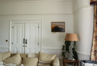 Elegant living room featuring a cream sofa, landscape painting, and ornate table lamp by white double doors.