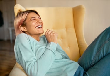 femme heureuse riant dans un fauteuil jaune.