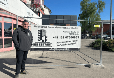 Geschäftsführer der Hebestreit Generalunternehmer GmbH vor Firmenbanner an einer Baustelle