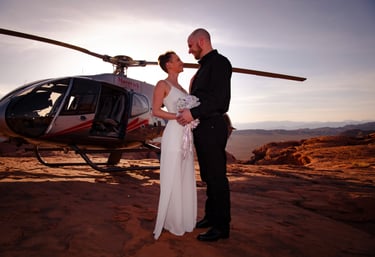 a bride and groom standing in front of a helicopter