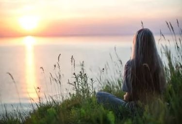 personne assise face au coucher de soleil illustrant la sérénité apportée par la sophrologie