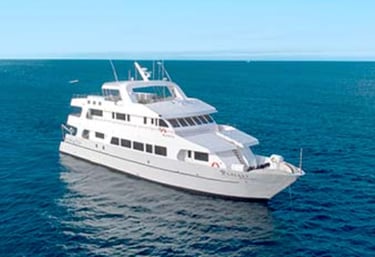 Small luxury cruise vessel anchored in a remote Galápagos bay at sunset