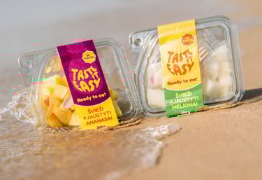 paplūdimyje ant smėlio padėti pjaustyto ananaso bei meliono indeliai