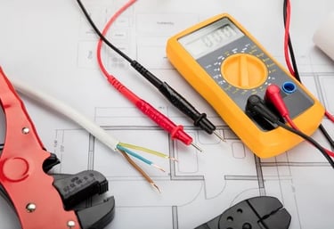 an image of a volt meter laying next to a splice of electrical wiring, laying on top of floor plansl