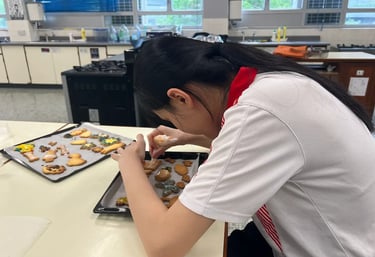 學生雙手擺放甜品於托盤上，動作認真細緻，畫面捕捉學習中的靜心與專注力量。