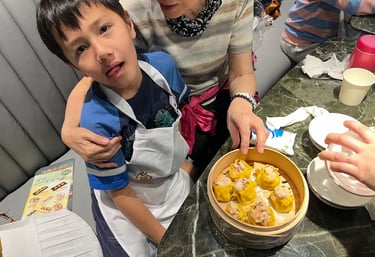 家長陪同孩子一同製作燒賣，雙手合作包裹餡料，展現親子參與與互相支持的溫馨互動。