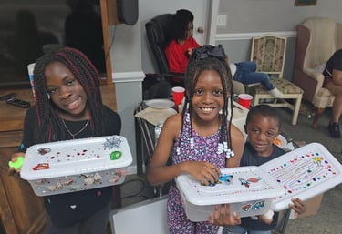 Three smiling children holding decorated plastic storage bins at a family craft event.