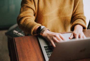 woman in yellow sweater typing on a laptop