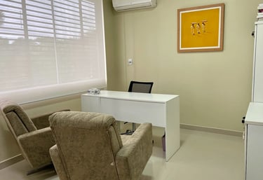 Um consultorio com uma mesa branca e duas poltronas.