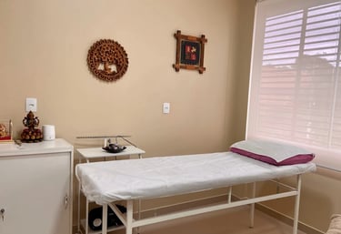 Um consultório com uma maca de terapia, alguns armários e quadros na parede.