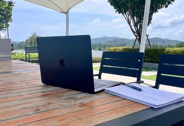 A Mac Laptop on a table, with the mountains of Phuket in the background