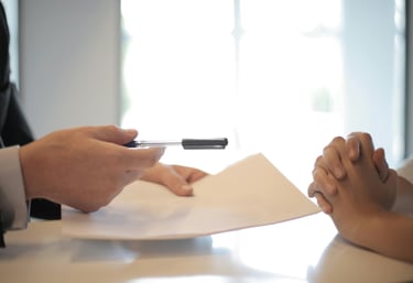 Duas pessoas sentadas à uma mesa, segurando papel e caneta.