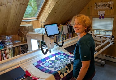 A smiling quilter standing in front of a longarm machine with a quilt in progress