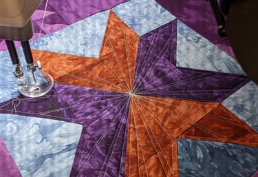 a closeup view of an orange an d purple quilt and the needle of a longarm machine