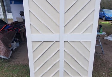 Custom white wooden sliding barn doors with a decorative chevron pattern outdoors.