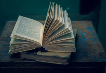 An open vintage hardcover book with fanned pages resting on an antique wooden table.