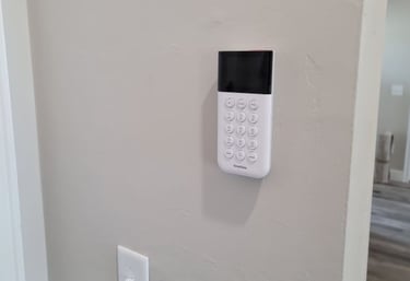 White SimpliSafe home security system keypad mounted on a neutral wall near a light switch.