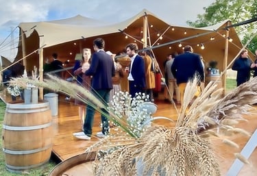 Invités discutant sous une tente stretch décorée de tonneaux, lors d’un mariage