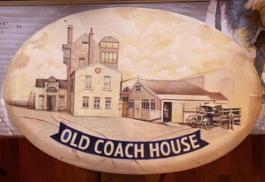 Oval pub sign with painted brewery buildings and name in blue ribbon.