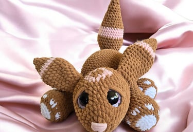 Handmade brown velvet bunny plushie with pink and white details, laying on soft pink satin fabric