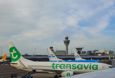 3 vliegtuigen van zowel Transavia als KLM op Schiphol met de verkeerstoren op de achtergrond