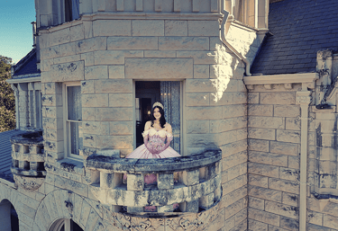 a woman in a pink quinceanera dress sitting on a balcony