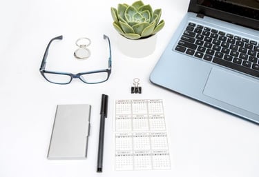 Minimal workspace with laptop, calendar, eyeglasses, and plant