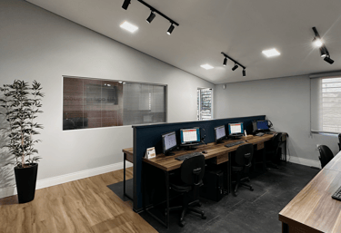 Modern office workspace with wooden desks, computer monitors, and track lighting in a minimalist call center.